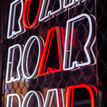 close up photo of red and white neon sign of the word ROAR over and over